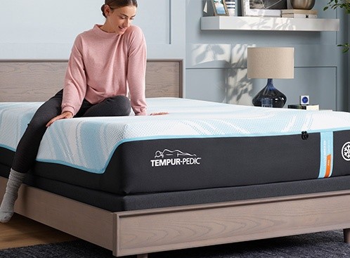 a person sitting on a Tempur-pedic LuxeBreeze Firm mattress in a well-lit room