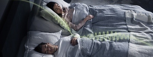 Man and woman comfortably sleeping together; the woman’s head is raised and there’s a green illustration that represents the smart technology of the base