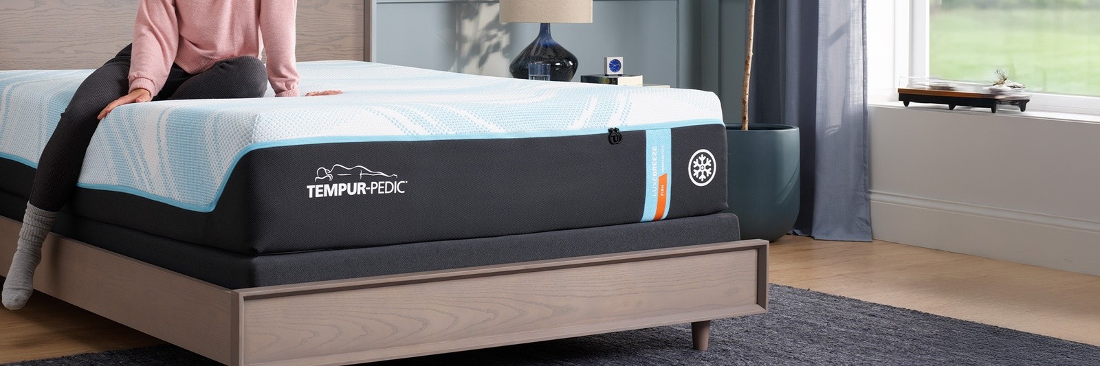 a person sitting on a Tempur-pedic LuxeBreeze Firm mattress in a well-lit room