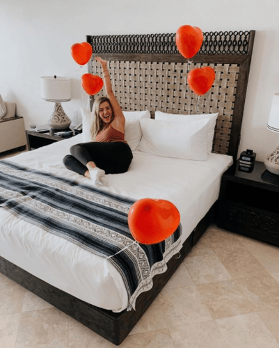 woman smiling while lying on decorated bed with woven headboard and heart balloons